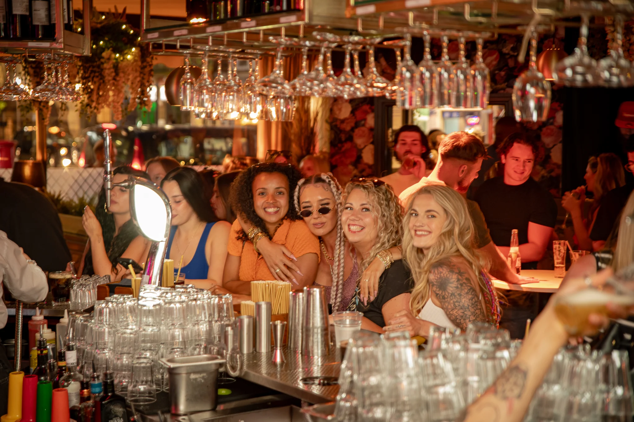 Friends smiling at the packed Baluga bar beneath hanging glassware