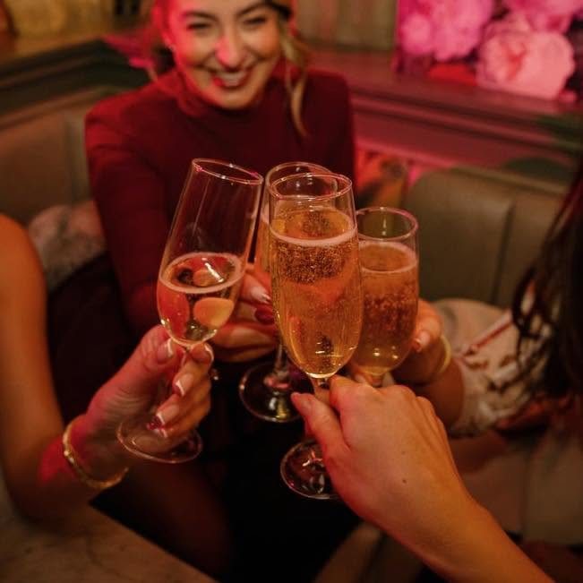 Friends clinking prosecco flutes in a booth at Baluga